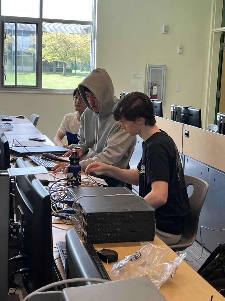 Three students work at a computer at a long row of desks