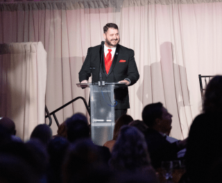 Alumni speaker Roger Dover speaks at a lectern on a curtained stage