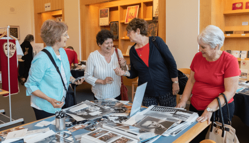 Four alumni share over a table filled with Saint Martin's photos and memorabilia from the archives