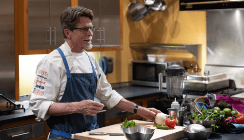 Chef Rick Bayless in kitchen in front of a cutting board and ingredients