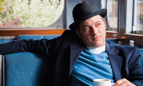 Jonathan Evison sits in a booth, looking out a window with a cup of coffee