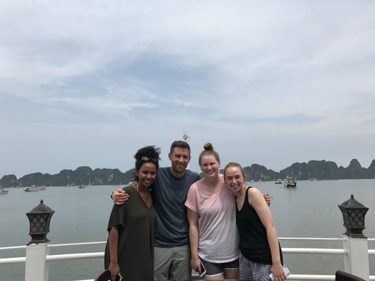 Students and professor at the railing of a ferry, with water and jagged hills behind