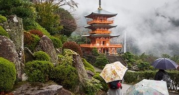 Japanese tiered building in a lush setting with fog behind and people with umbrellas