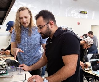 Dr. Picone assists a student with work on technology while other students are working similar projects behind them.