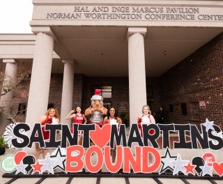Cheerleaders and Marty stand behind a giant Saint Martin's Bound sign, bubblies floating in the air