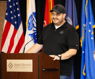 A student stands at a podium in front of American and military flags