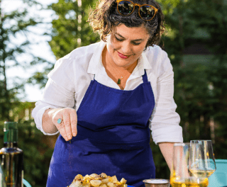 Chef Renee Erickson sprinkles something onto food in a woodland setting