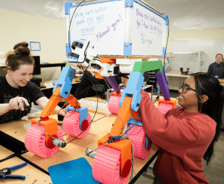 Two students work on a colorful machine