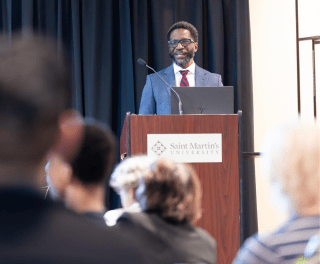 A student in a suit speaks from a podium to an audience