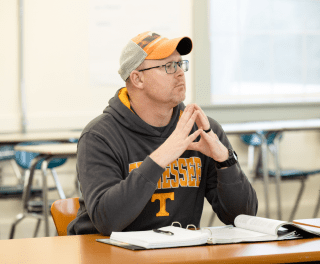 A student listens with steepled hands at a desk