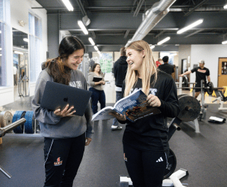 Two students examine a textbook in a weight room
