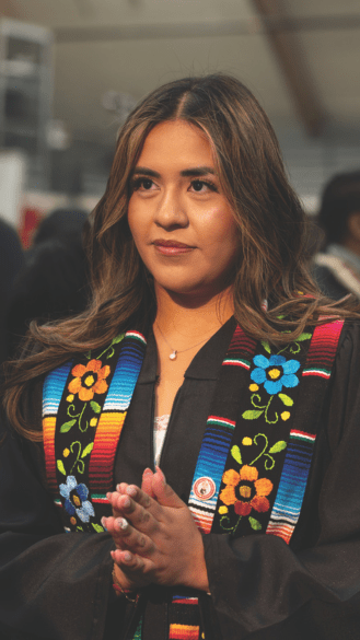 A student in graduation robes puts her hands together in prayer