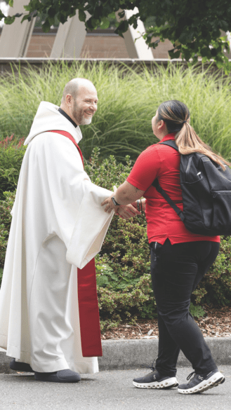 Fr. Peter in priestly robes shakes hands with a student