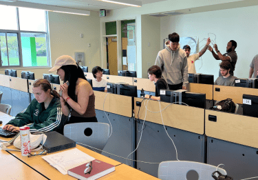 Students work in a computer classroom, cables crossing desks to create a network