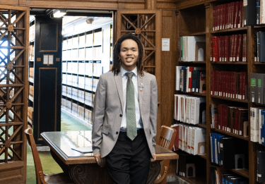 Student in a suit standing in wood-paneled library