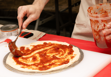 Red sauce being spread on pizza dough