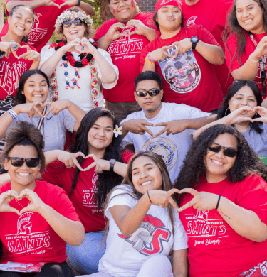 A large group of Saints in red smile and make hearts with their hands, with the president