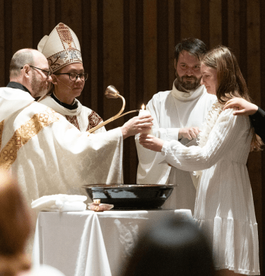 The abbot and other religious community members stand with student in white over baptismal fount