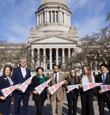 Students and the president stand in front of the Olympia capitol building holding pennants