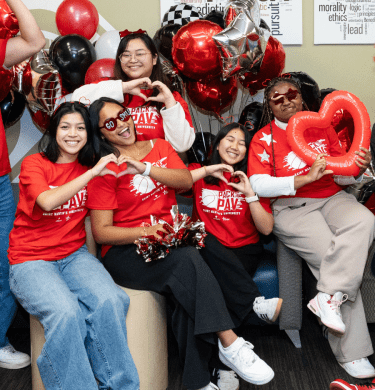 Students in red shirts gather and make hearts with hands