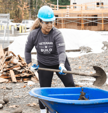 Student in hard hat shovels into a wheelbarrow on a construction site