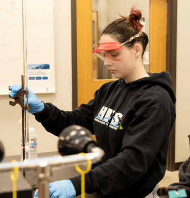 A student in protective goggles conducts an experiment