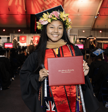 A student in graduation regalia holds their diploma at commencement