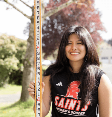 A student in a Saints soccer shirt holds a long measuring stick outside