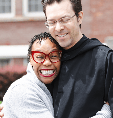 Two folks side hug in front of a brick building