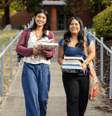 Two students walk down from the library carrying stacks of books