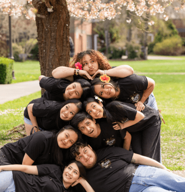 Students in black tshirts pose under a blossoming tree