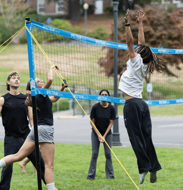 A student jumps while playing volleyball outside