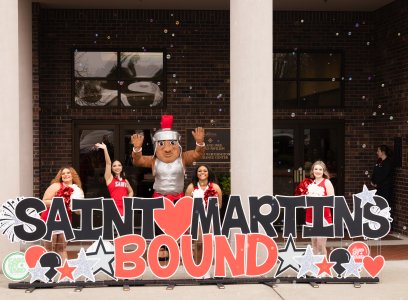 Marty and cheerleaders wave behind a large sign saying "Saint Martin's Bound," bubbles in the air