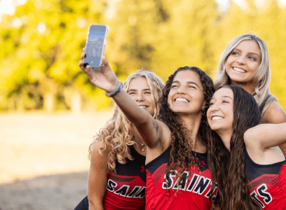 A group of students in red Saints shirts pose outside for a selfie