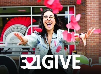 A student scatters red tickets in the air above the 3.21GIVE logo