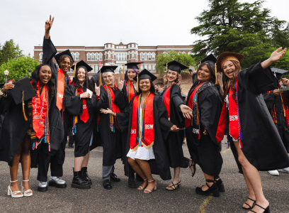 Students in graduation gowns pose with Old Main in the background
