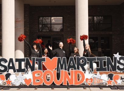 A monk and some cheerleaders wave from behind a huge sign that says Saint Martin's Bound