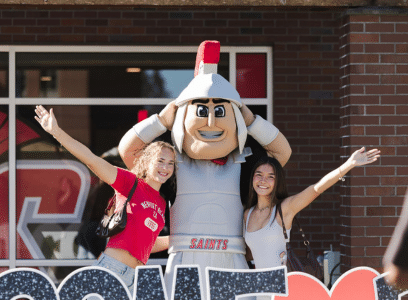 Students pose with Marty the Mascot in front of a brick building