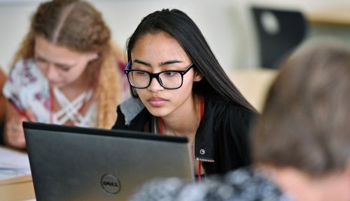 A student works at a laptop, other students working around her.