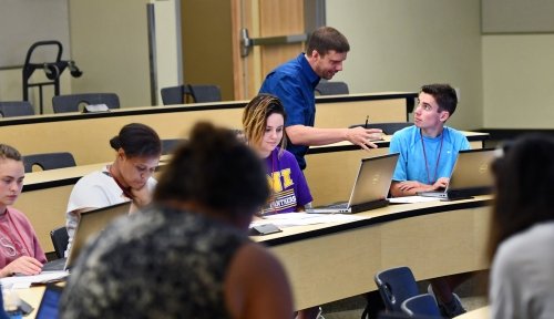 Dr. Aaron Coby assists students sitting in a lecture hall.
