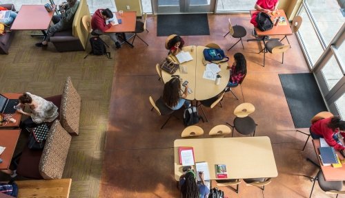 Overhead view of sitting area in Harned hall with lots of students grouped at various tables working alone or in company.
