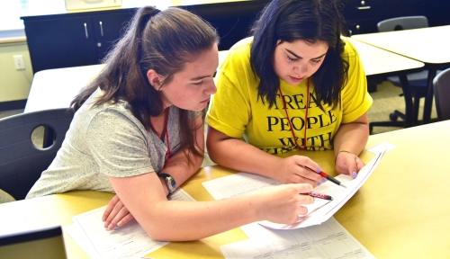 Two students seated at a desk work on a paper.