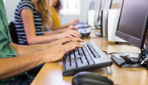 Students type on keyboards at a row of computers.