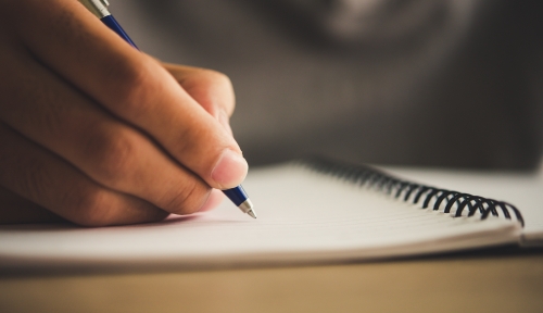 Close up of hand holding a pen writing in a spiralbound notebook.