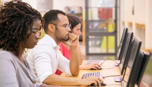 Three students work at a row of computers in a computer lab.