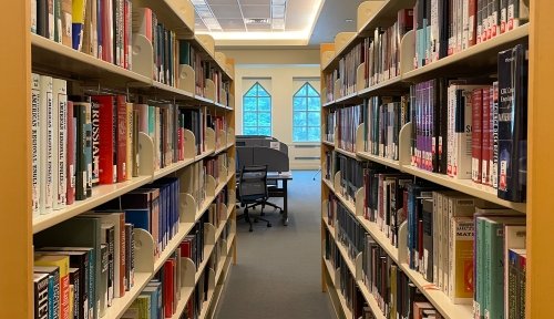 Interior shot of the library, looking down an aisle with cases of books on either side.