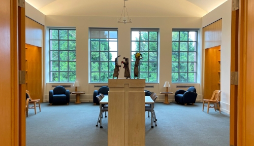 Interior shot of the library with windows in the background and statues in the middle on top of a row of carrells and chairs.