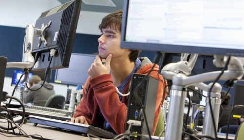 A student strokes their chin while working at a computer in a computer lab.