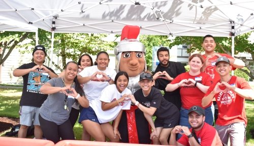A large group of students pose with the SMU Saint mascot, making hearts with their hands