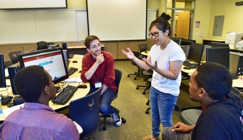 Dr. Floraliza Bornasal addresses a group of three students in a computer lab, advising them on class schedules.